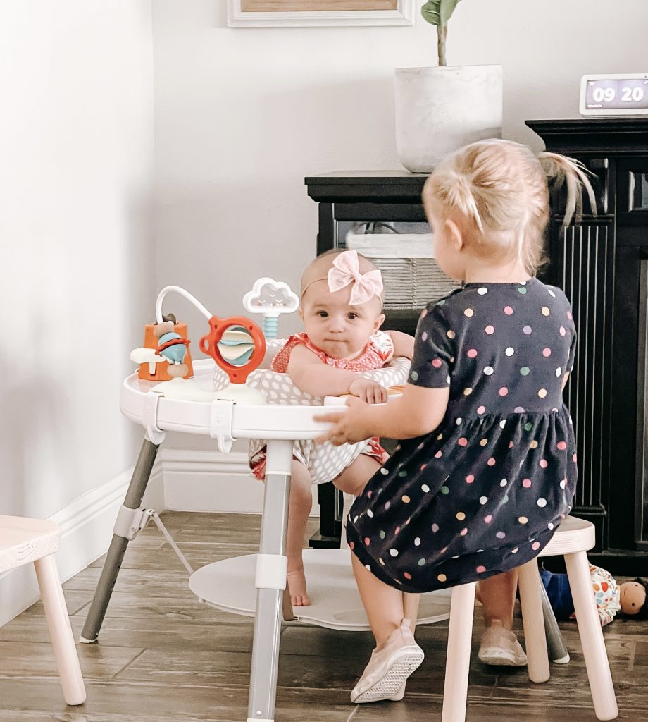 toddler girl sitting on a stool playing with an infant girl